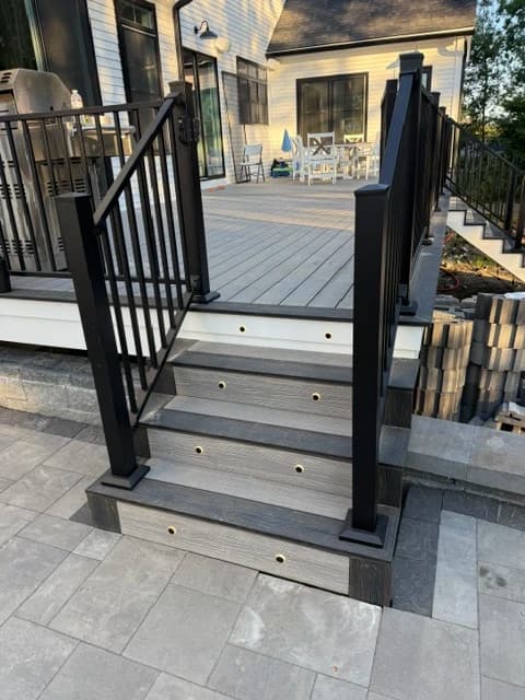 Composite deck stairs with gray decking boards, black aluminum railing, and stone paver landing