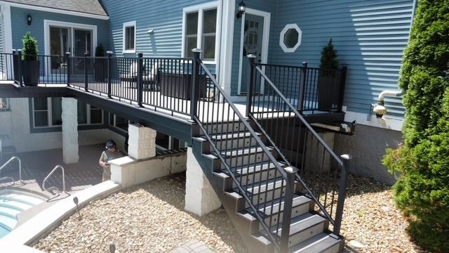 Ground-level view of composite deck with wide staircase and black aluminum railing beside a pool