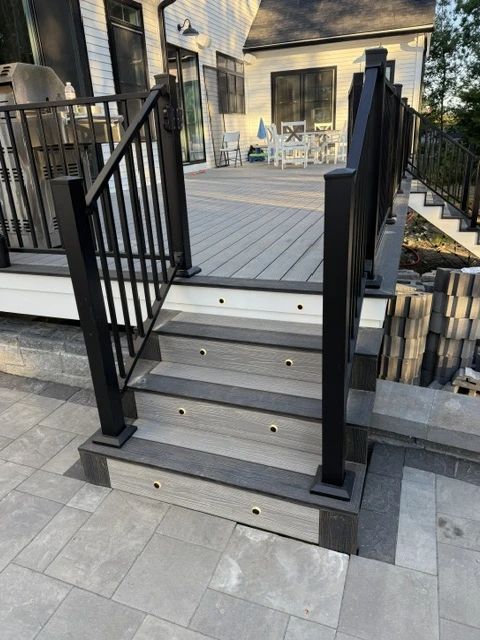 Composite deck stairs with gray decking boards, black aluminum railing, and stone paver landing